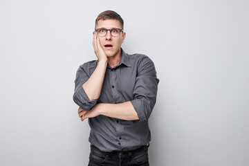Shocked man with hand on cheek standing against white background expressing surprise and disbelief