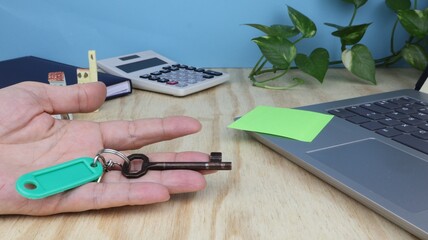 Hand holding house keys on desk background with objects and green climbing plant. series of photos.