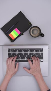 Top Shot View of a Desk With a Laptop, Notebook and Cup of Coffe on it Showing Hands Typing on a Keyboard, Vertical Video