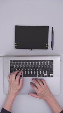 Top Shot View of a Desk With a Laptop and Notebook on it Showing Hands Typing on a Keyboard, Vertical Video