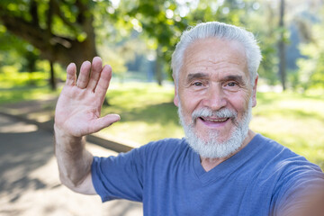 Engaging portrait of a joyful elderly man waving hello in a sunny park, capturing a moment of...