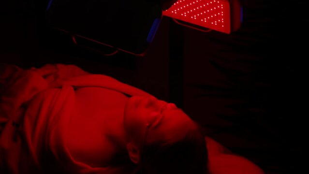 Close-up face of female client lying during non-invasive type of phototherapy. Closeup of woman patient in protective goggles undergoes blue LED light therapy for skin rejuvenation at aesthetic clinic