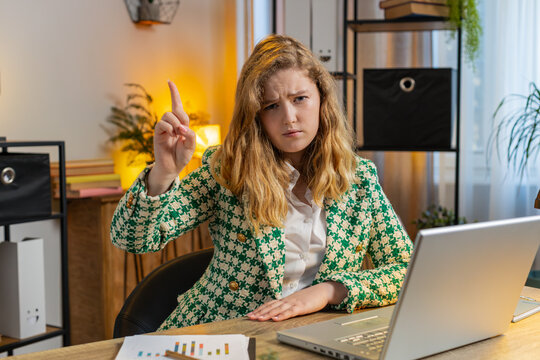 Young Caucasian businesswoman working on laptop shakes finger and saying No be careful scolding and giving advice to avoid danger mistake disapproval sign at home office. Freelancer woman at table.