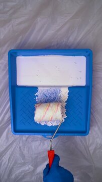 Paint Roller With White Paint Into a Blue Paint Tray on Protected Background, Vertical Video