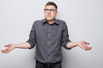 Confused young man shrugging shoulders against a gray background