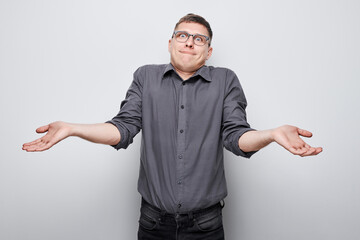 Confused young man shrugging shoulders against a gray background
