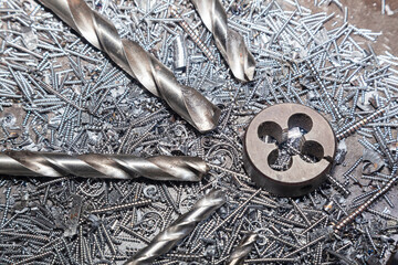 Drill bits for drilling steel lie on steel shavings close-up. Thread cutting die - obrazy, fototapety, plakaty