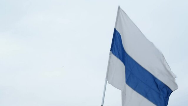 The flag of free Russia, the symbol of the opposition, blue white stripes, flutters in the wind against a cloudy gray sky. A rally in support of Ukraine and against the Russian government and the war