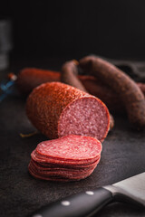 Sliced smoked salami sausages on black table.