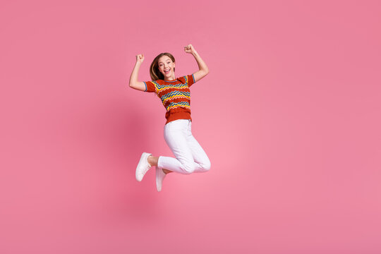 Full length portrait of delighted nice person jumping raise fists accomplish empty space isolated on pink color background