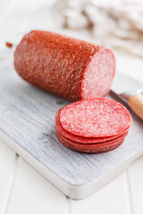 Sliced smoked salami sausages on cutting board on white table.