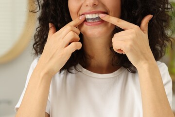 Young woman applying whitening strip on her teeth indoors, closeup