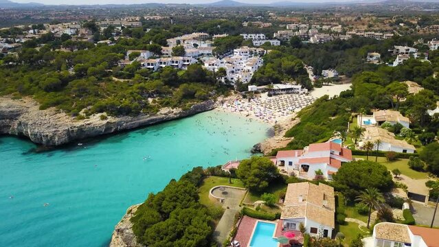 Cala anguila with crystal clear waters, beachgoers, and surrounding villas, sunny, aerial view