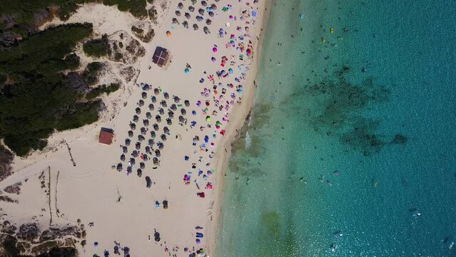 Cala agulla beach with vibrant umbrellas, clear water, and parked cars, aerial view