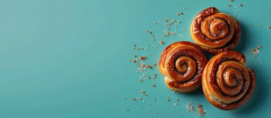 Three homemade cinnamon buns are neatly arranged on a vibrant blue background, showcasing their delicious swirls and sweet aroma.