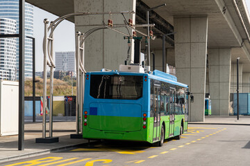 Electric bus at a stop is charged by pantograph. Clean mobility.