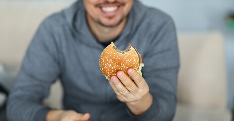 Focus on male hand holding big tasty hamburger full of mischievous calories and harmful...