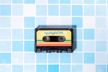 Top view of a music cassette on a background of light blue retro-style squares.