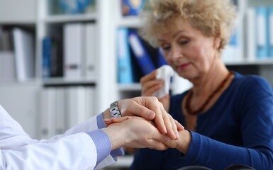 Focus on male hands of doctor holding arms of sick elderly woman. Therapist supporting and calming ill granny. Health care, treatment and medicine concept