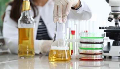 Close-up of assistant hands pouring yellow liquid into flask. Professional scientist making mixture of fluid for experiment. Chemical researching and quality test concept