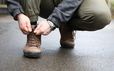 Close-up view of male hands sitting down outside on street and tying shoelaces on sneakers. Person...