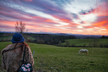 Coucher de soleil avec une femme admirant le paysage et un cheval dans un champ