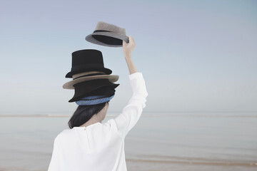 surreal woman from behind adds another hat on her head to the tower of hats she already wears,...