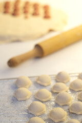 Fototapeta na wymiar cooking dumplings on the kitchen table there is a wooden rolling pin with dough and raw dumplings