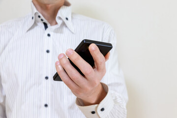 片手にスマートフォンを持つ白いシャツ姿の男性