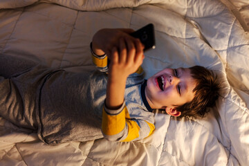 Boy searching the internet at home at night. Cute little boy sitting in the dark and watching cartoons on mobile.