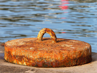 An old anchor encrusted with rust at the edge of the wharf against blue waters