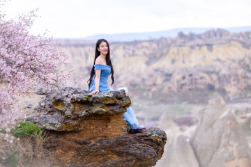 Beautiful woman in blue dress on rocks mountain. Cheerful woman relax outdoor with beautiful sky and pink flowers in holiday vacation. Woman tourist enjoy amazing mountain view. Travel and freedom..