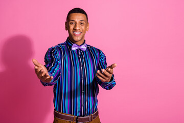 Photo of positive excited guy dressed striped shirt inviting you come empty space isolated pink...