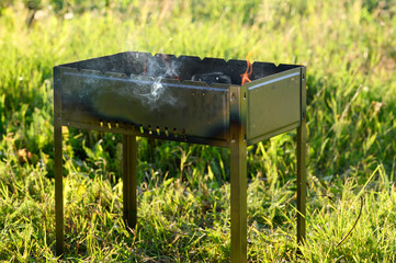 Black metal brazier with firewood and coals for a picnic, barbecue on a summer sunny day in nature....