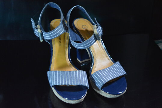 Stylish and unusual women's shoes made of blue genuine patent leather and blue fabric. Sandals, sandals, flight shoes are located on a black glossy background.