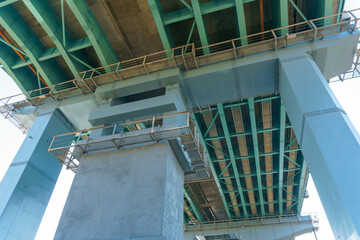 Parts of a modern metal bridge in close-up against a blue sky background. Metal structures connected by large bolts and nuts to a reinforced concrete base. Railway or automobile bridge.