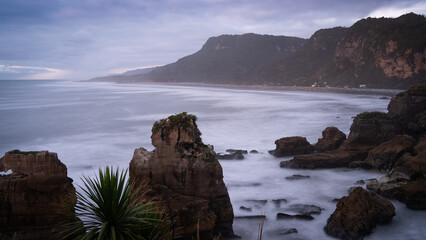 Rough ocean coast with waves and some houses and sharp cliffs during sunset, New Zealand