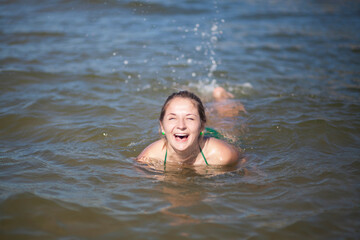 A woman splashes in the water, splashes flying in all directions. The woman smiles broadly and...