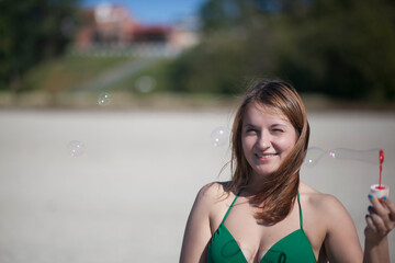 A woman in a green bikini swimsuit launches soap bubbles on the beach