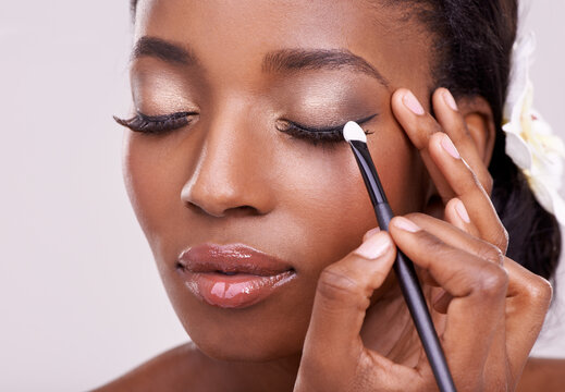 Black woman, face and brush for eyeshadow with beauty, makeup and lashes on grey background. Skin glow, hands and apply cosmetic product with tools for cosmetology, shimmer or glitter with shine