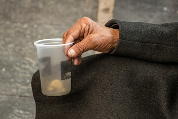 Closeup of a man's hand grasping a plastic cup and asking for donations.