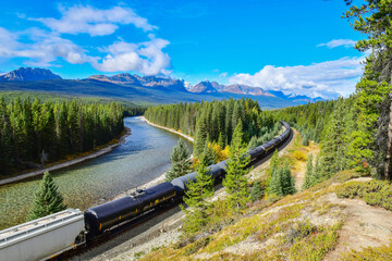 Long freight train moving along Bow river in Canadian Rockies ,Banff National Park, Canadian Rockies,Canada. - obrazy, fototapety, plakaty