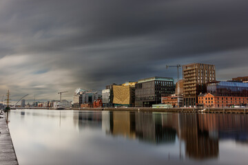 Fototapeta na wymiar Dublin, Ireland, Dockland, modern building business center cityscape by Liffey river view during sunny day with tall ship and Samuel Beckett bridge in background. europe