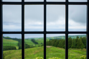 Window with iron grille and in the background the green fields of the Azores. Sao Miguel island in the Azores. Selective Focus.