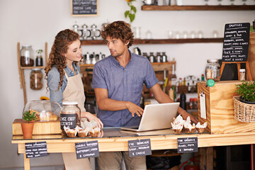 Computer, bakery and small business people with team for of sales, planning and advice in startup. Young woman and man or water in review for inventory, profit and e commerce on laptop at cafe