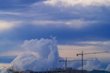 Landscape with contrasting dark blue clouds and with the tops of new buildings and two construction cranes. Amazing conditions of the surrounding nature, weather