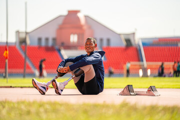 Asian para-athlete relaxes and Warm-up runner prosthetic leg on the track alone outside on a stadium track Paralympic running concept.