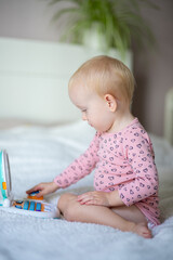 Toddler playing with a toy laptop on a bed with a plant in the background.