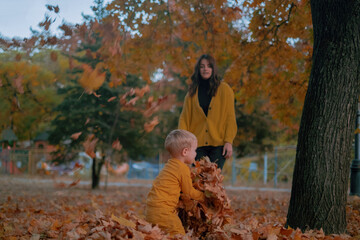 A mother and son spend quality time together, playing in the autumn park, both dressed in yellow...