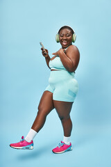 Fototapeta na wymiar plus size african american woman listening music in headphones connected to smartphone